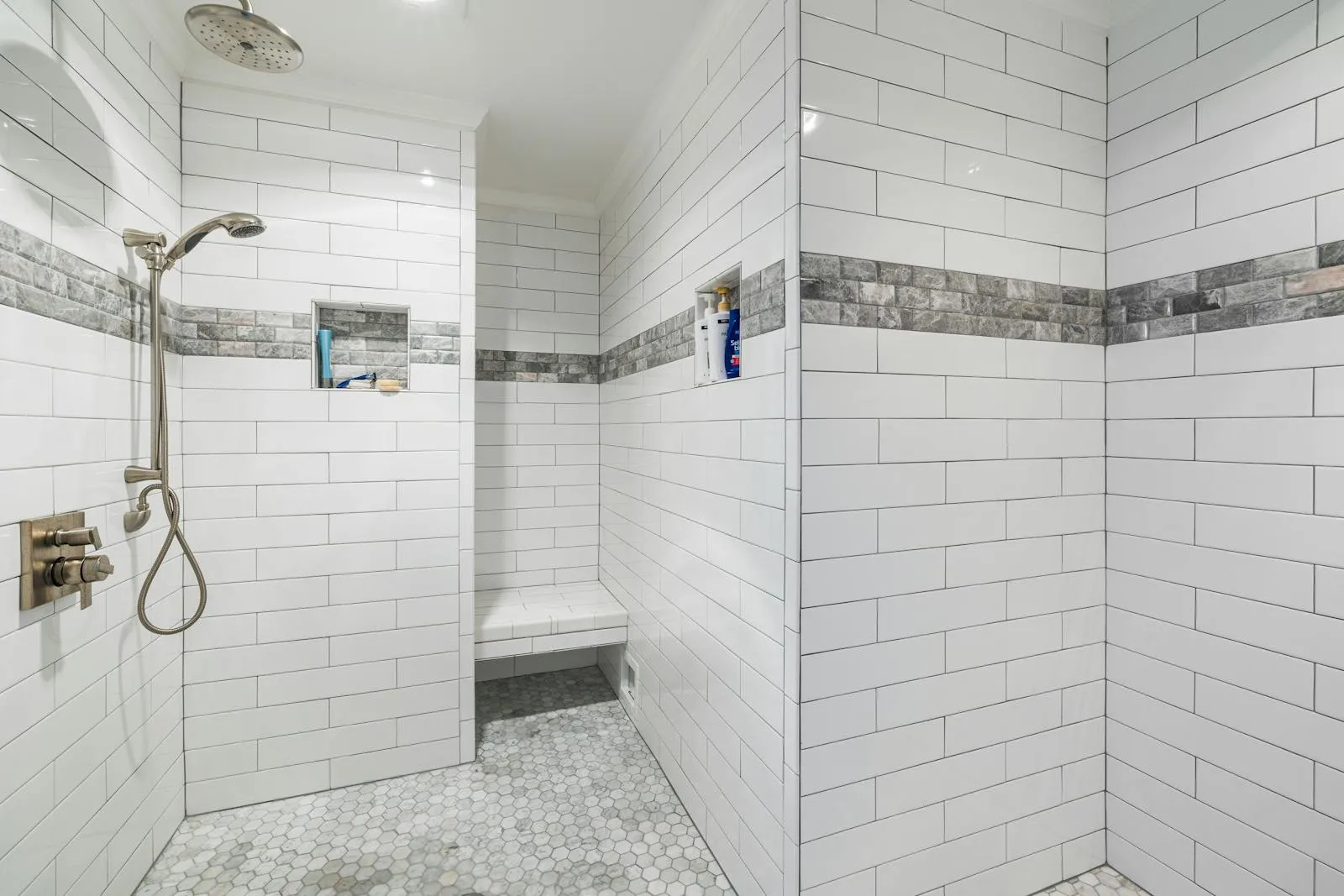 A finished walk-in shower with white metro tiles and a stone feature band