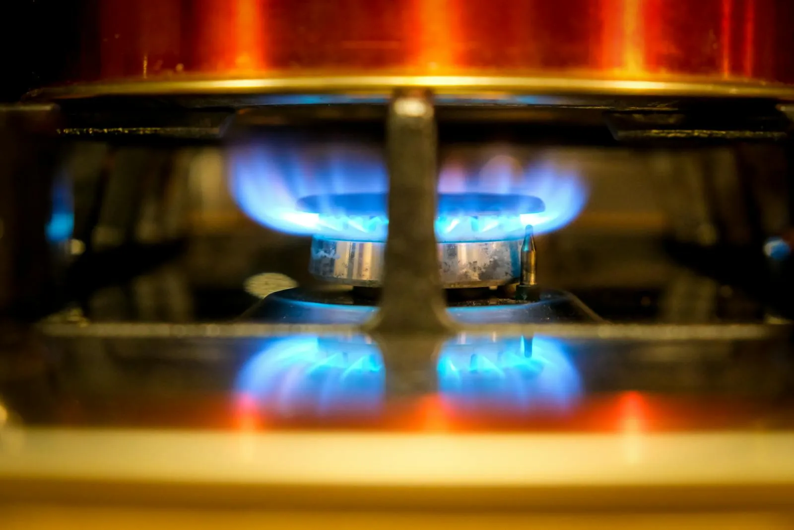 A lit gas burner with a clean blue flame underneath a pan